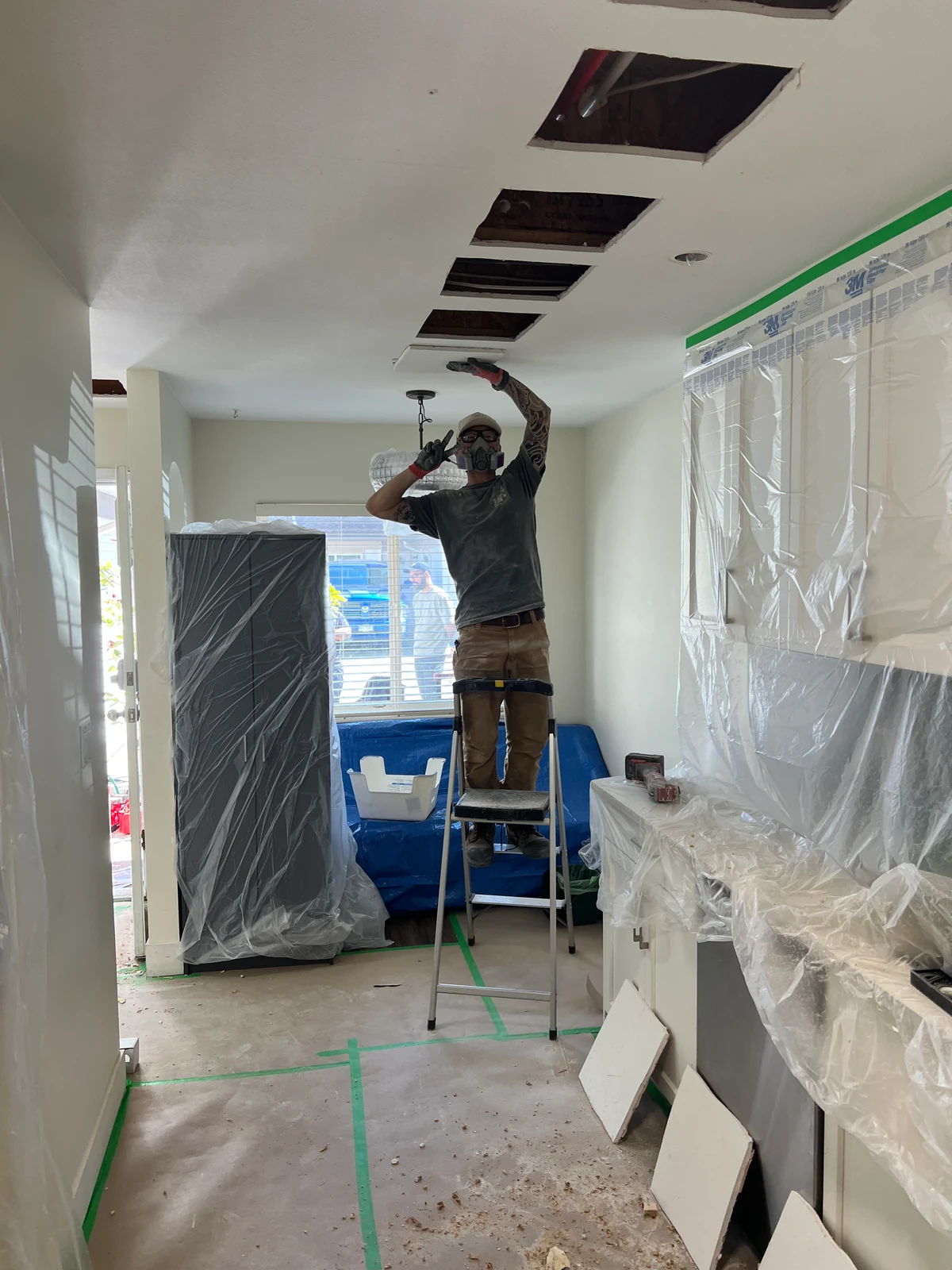 Technician working through ceiling openings above protected furnishings in the Surrey repipe project