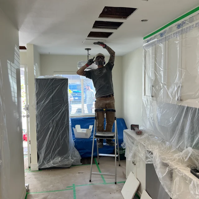 Technician working through ceiling openings above protected furnishings in the Surrey repipe project